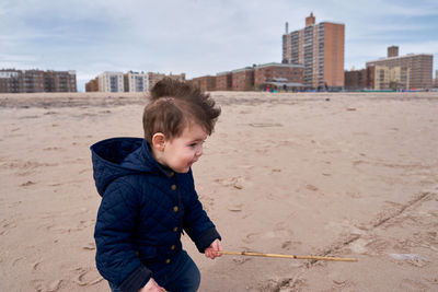 Happy young toddler running around the beach with a big branch