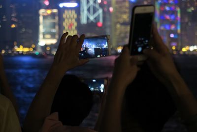 Midsection of woman photographing illuminated mobile phone at night