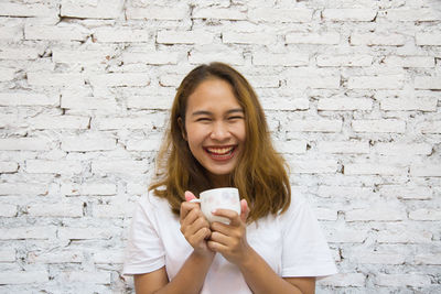 Portrait of smiling woman with coffee cup against wall