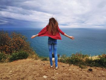 Rear view of woman standing by sea against sky