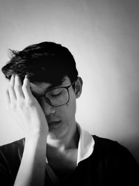 Close-up of young man with eyes closed wearing eyeglasses against wall