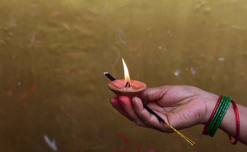 Cropped hand of woman holding lit diya and incense