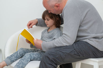 Rear view of father and daughter sitting on floor