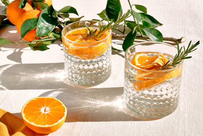 Summer refresh orange cocktail with ice, herb and ripe bio citrus fruits on linen tablecloth. 