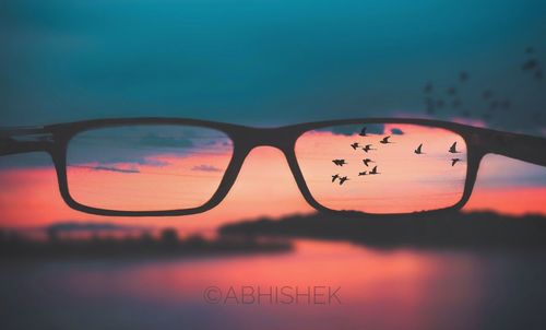 Close-up of sunglasses against sky during sunset