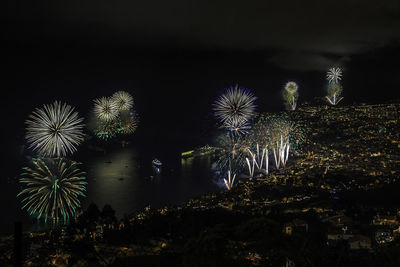 Aerial view of firework display over sea and illuminated madeira island at nigh