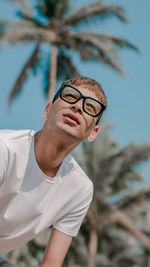 Young man looking away while wearing eyeglasses against trees and sky