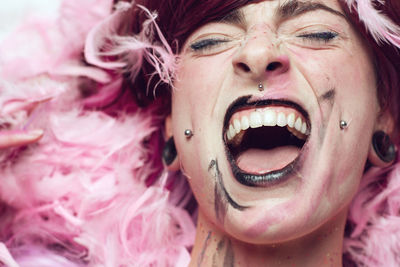 Close-up of woman with make-up screaming amidst pink feathers