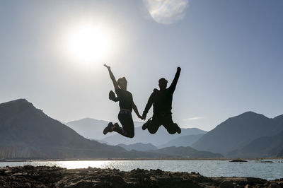 Couple jumping and enjoying a natural landscape of mountains and lake.