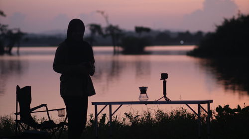 Silhouette woman standing by lake against sky during sunset