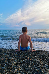 Child sits on the seashore, view from the back