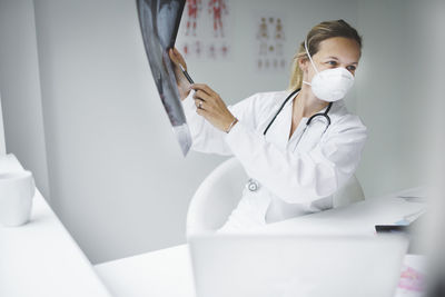 Female doctor wearing mask holding medical x-ray in hospital