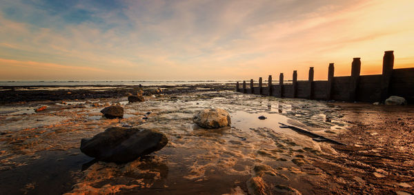 Wooden posts on beach against sky during sunset