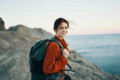 Portrait of smiling young woman standing on sea shore against sky