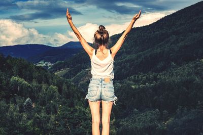 Rear view of woman with arms raised standing against mountains