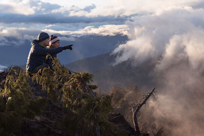 Side view of mother and son sitting on cliff against mountains