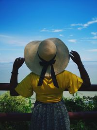 Rear view of woman standing by hat against sky