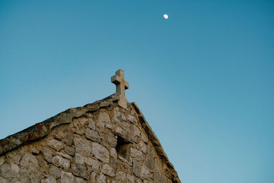 Low angle view of bird perching on roof against clear blue sky