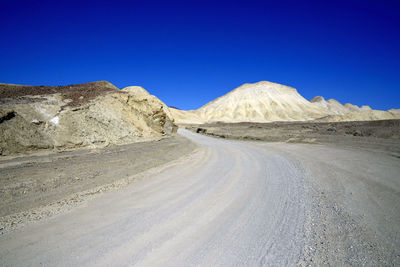 Road leading towards mountains against clear blue sky