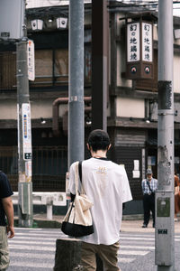 Rear view of man walking on street against buildings in city