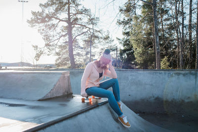 Woman sat on a board in a skatepark in the sunshine