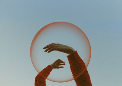 Cropped hand amidst bubble against sky