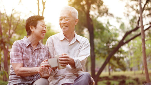 Smiling couple having drink while sitting in park