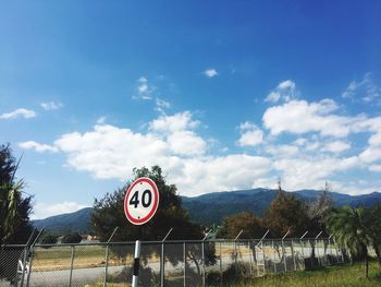 Road sign by trees against sky