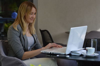 Smiling woman using laptop while sitting on chair at home