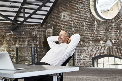 Smiling businessman sitting at table in a loft leaning back