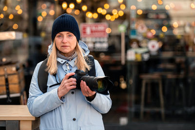 Blonde middle-aged woman with a photo camera in the evening on the city streets, lifestyle concept