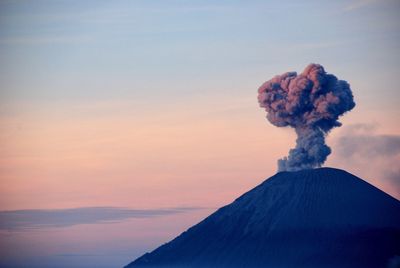 Smoke emitting from volcanic mountain against sky during sunset