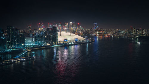 Illuminated buildings by river against sky at night