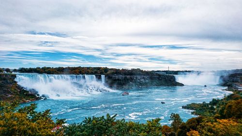 Scenic view of waterfall against cloudy sky