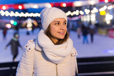 Portrait of smiling young woman standing in illuminated park during winter