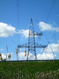 Electricity pylon on grassy field against cloudy sky