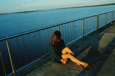 Full length of lonely woman sitting by railing on promenade