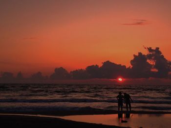 Silhouette couple standing at beach during sunset