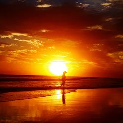 Silhouette man standing on beach against orange sky