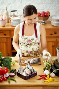 Beautiful woman cleaning fish in kitchen