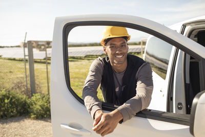 Portrait of young smiling male engineer leaning on van door at power station