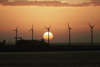 Silhouette windmills on field against sky at sunset