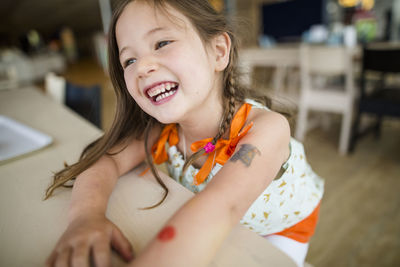 Close-up of happy girl looking away while sitting by wooden table at home