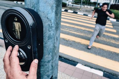 Cropped hand pushing button of traffic light control box while man running on street