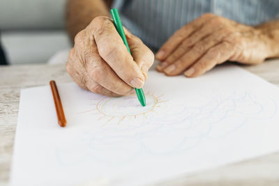 Senior man's hand drawing with green pencil, close-up