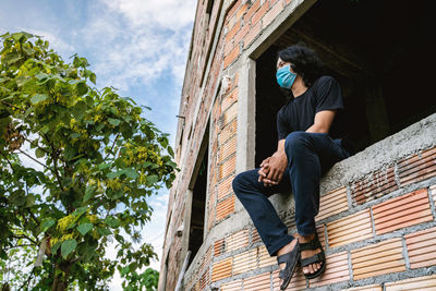 Low angle view of young man sitting against building