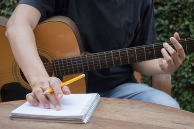 Midsection of men writing on diary while playing guitar