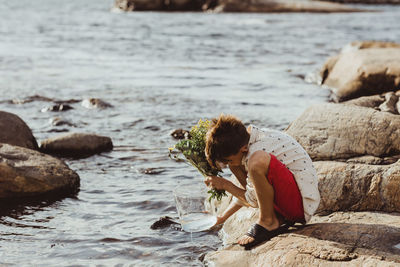 Boy crouching over rock while filling water in container during weekend