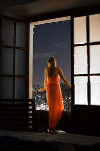 Rear view of young woman standing in balcony seen through doorway