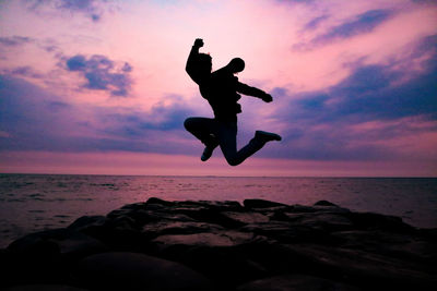 Silhouette man jumping on rock at beach during sunset